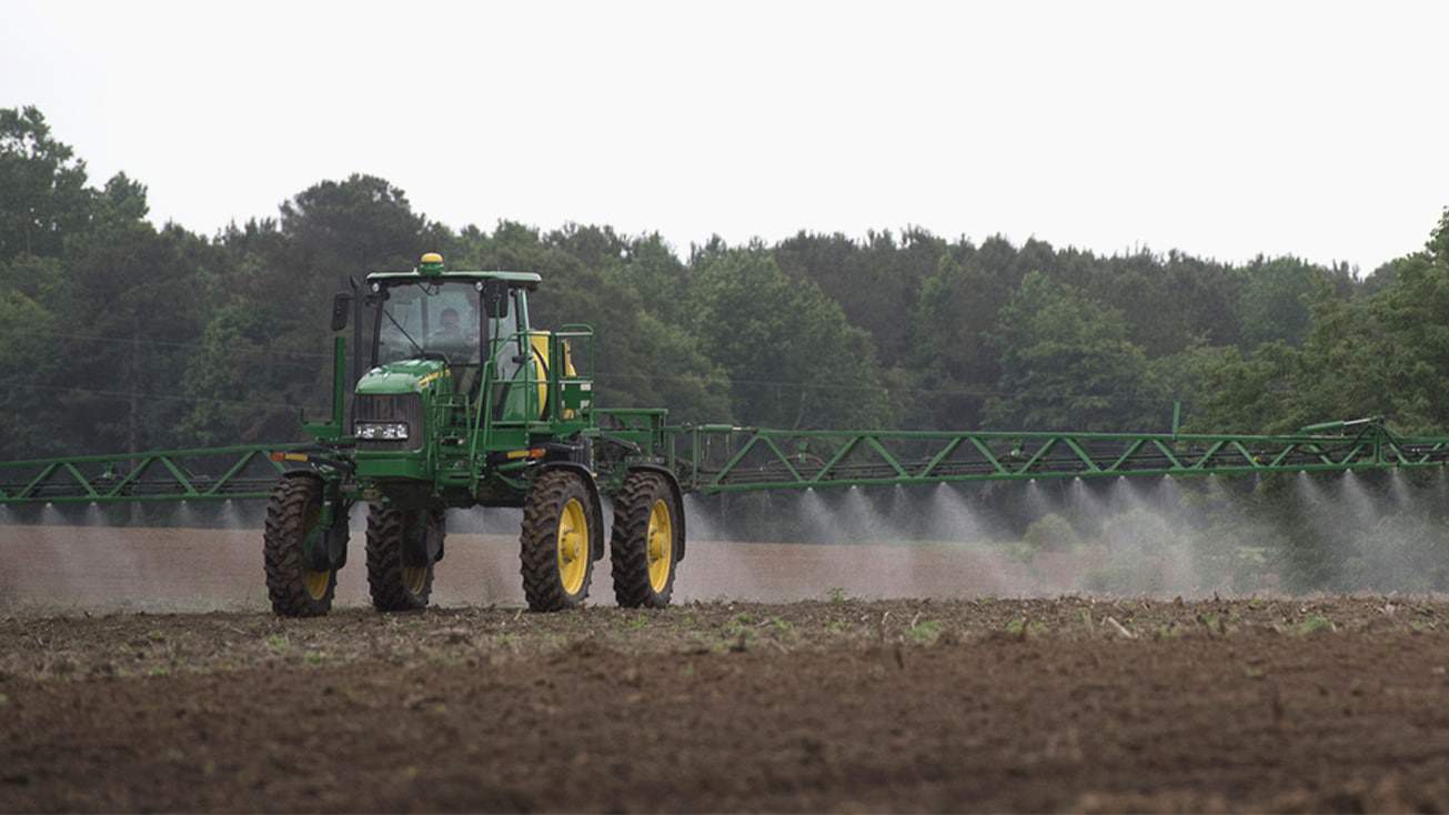 A tractor utilizing a sprayer to spray a field.