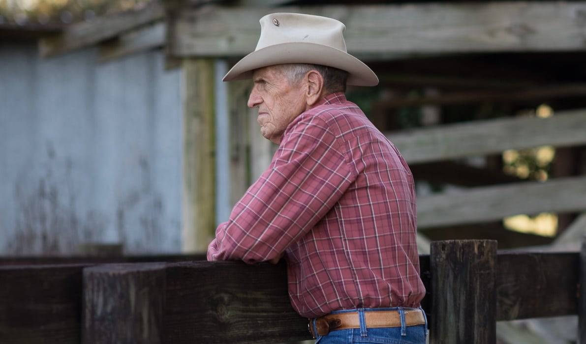 A man in a cowboy hat leaning on a fence, showcasing the beauty of agricultural crop diversification.