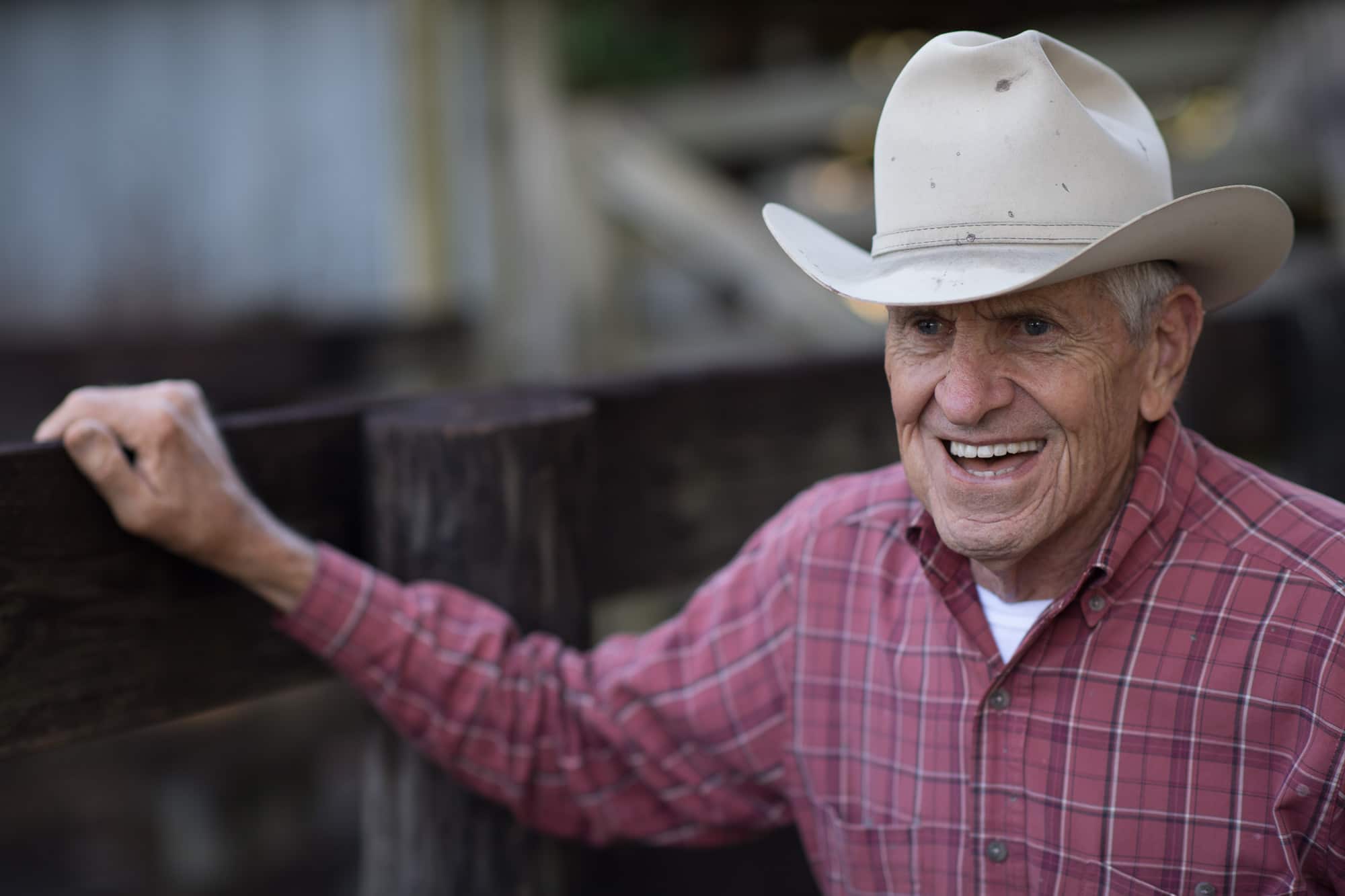 farmer with cowboy hat leaning against a wooden fence