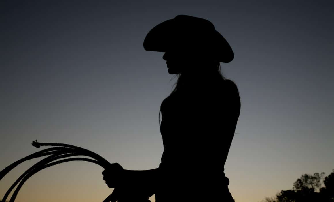 A silhouette of a female cowgirl holding a lasso.