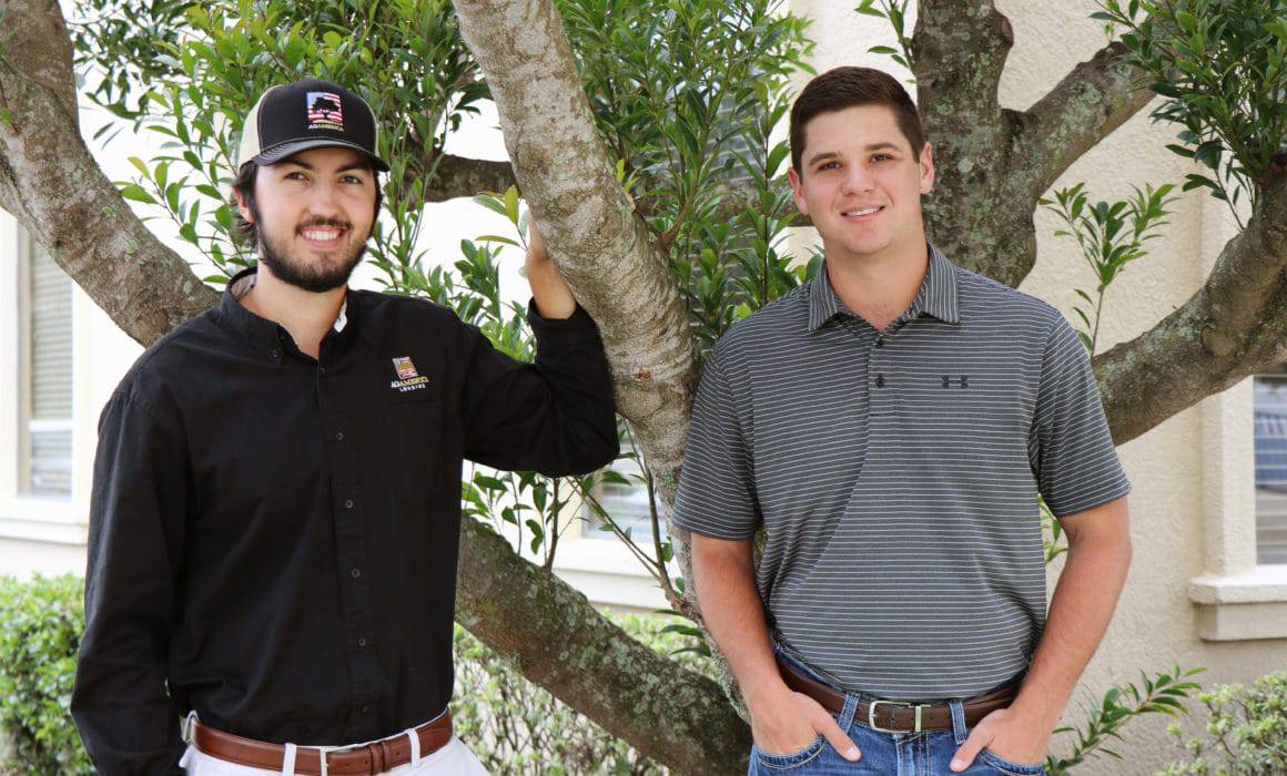 Two men engaged in agribusiness standing in front of a tree.