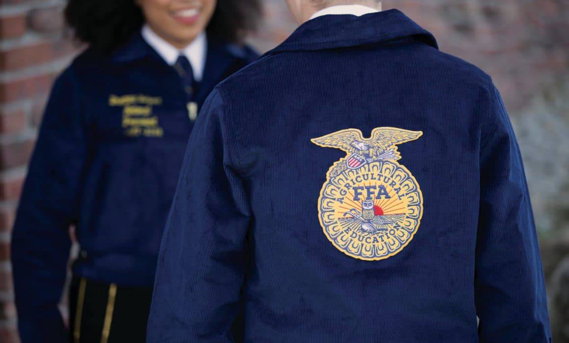 Two people wearing blue jackets in a classroom setting, with an eagle embroidered on them, representing their involvement in Agricultural Education.