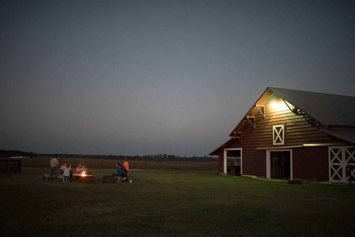 A family sitting around a fire pit in front of a red barn.