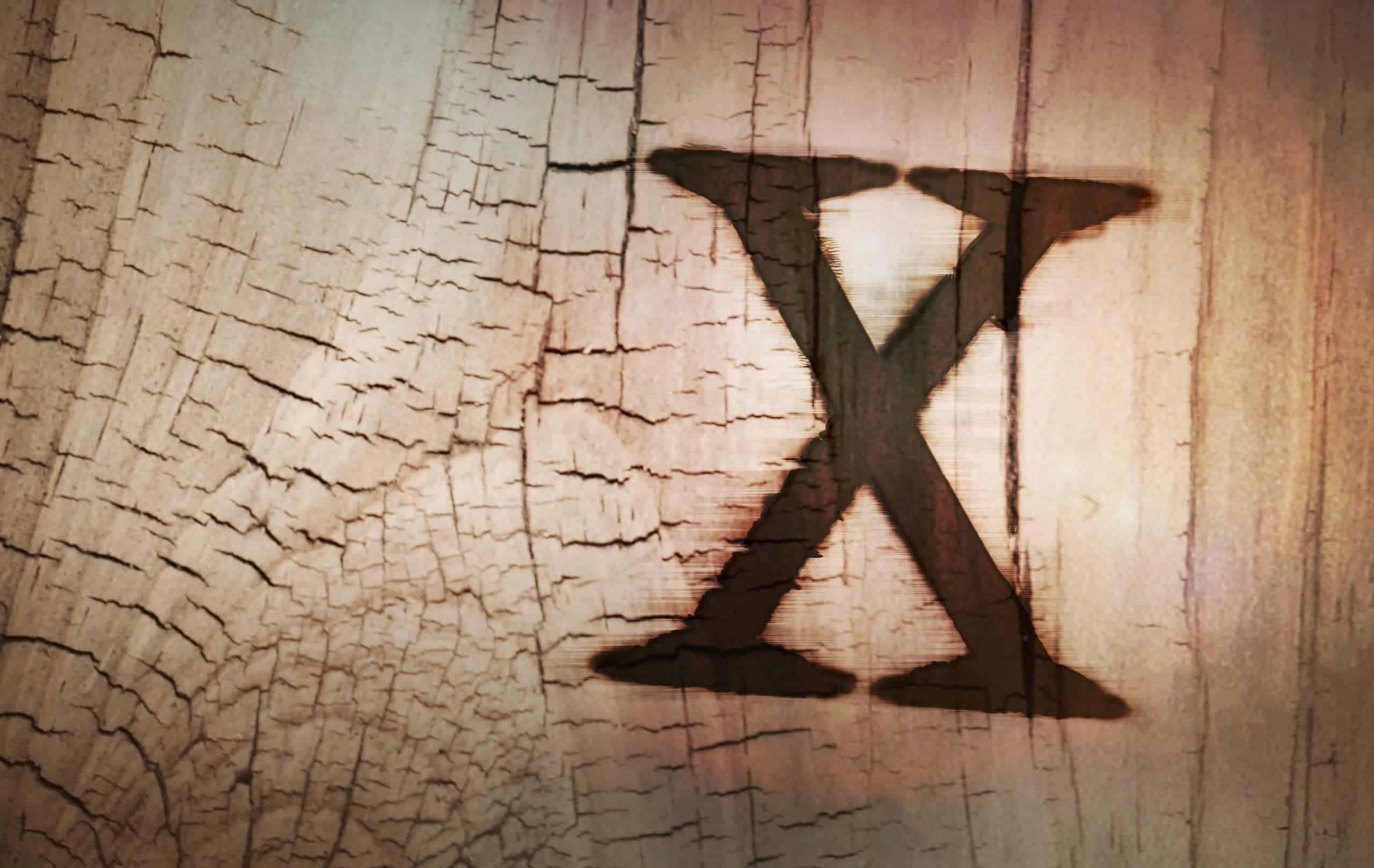 The letter x is painted on a piece of wood and displayed as an artistic representation.