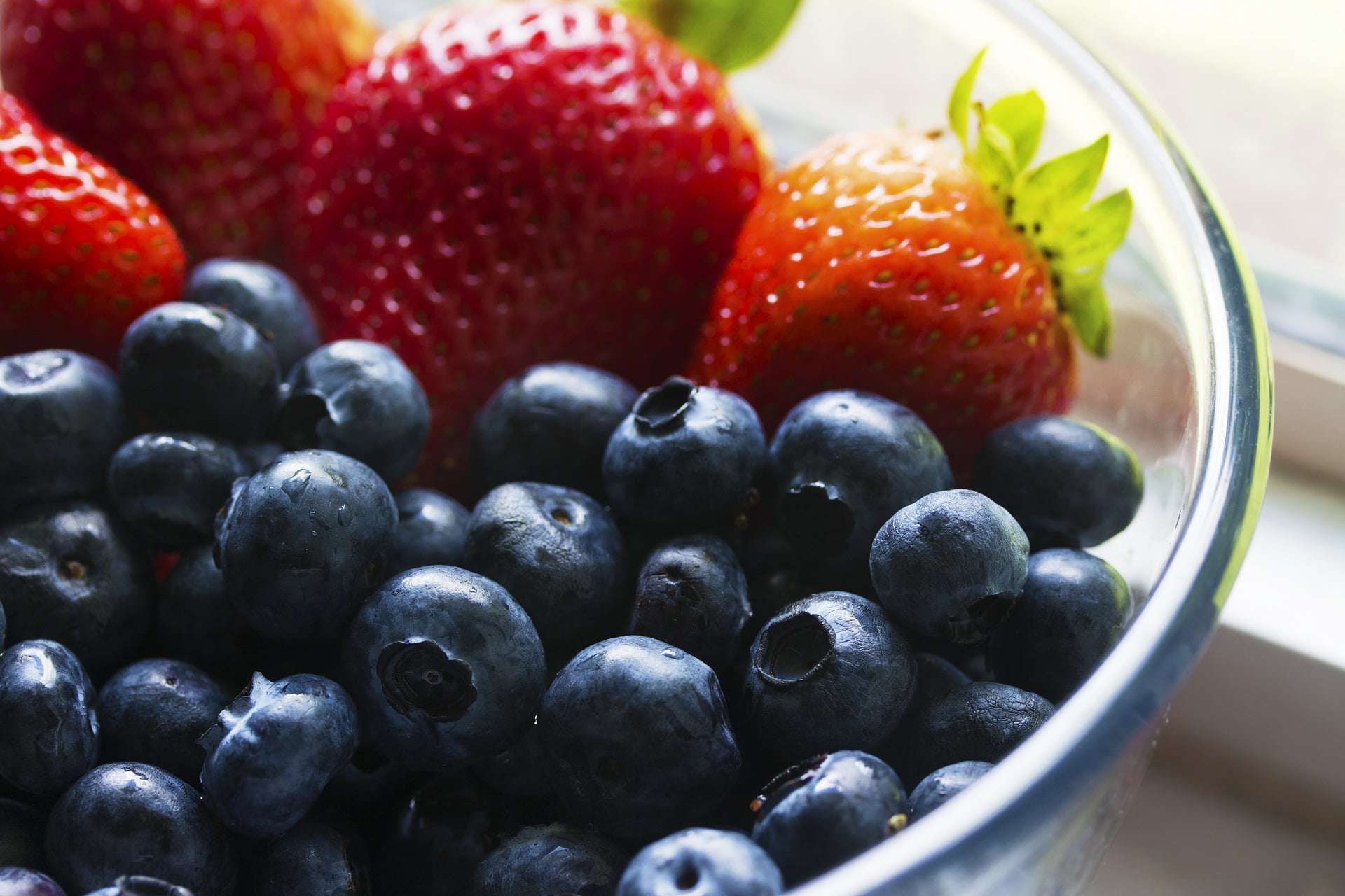 Blueberries and strawberries in a bowl on a window sill.