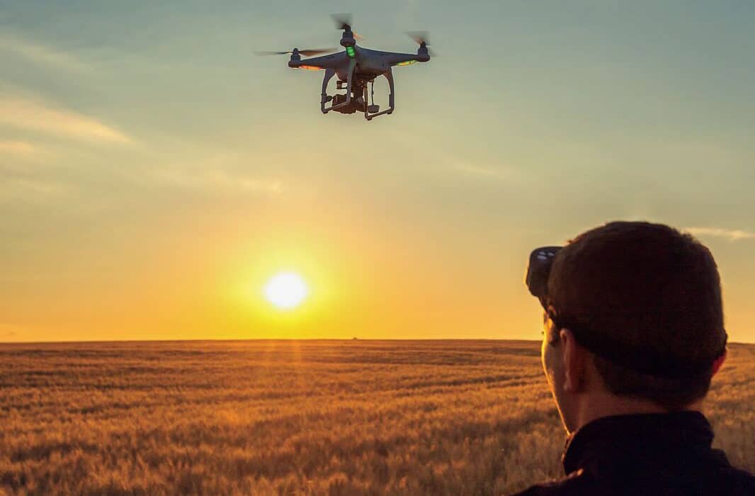 A man observing a drone conducting precision agriculture over a field at sunset.