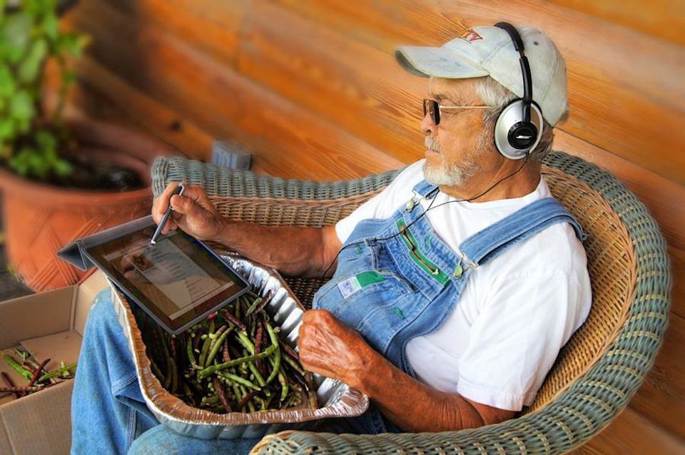 A man immersed in Ag News, sitting in a wicker chair with headphones and a tablet.