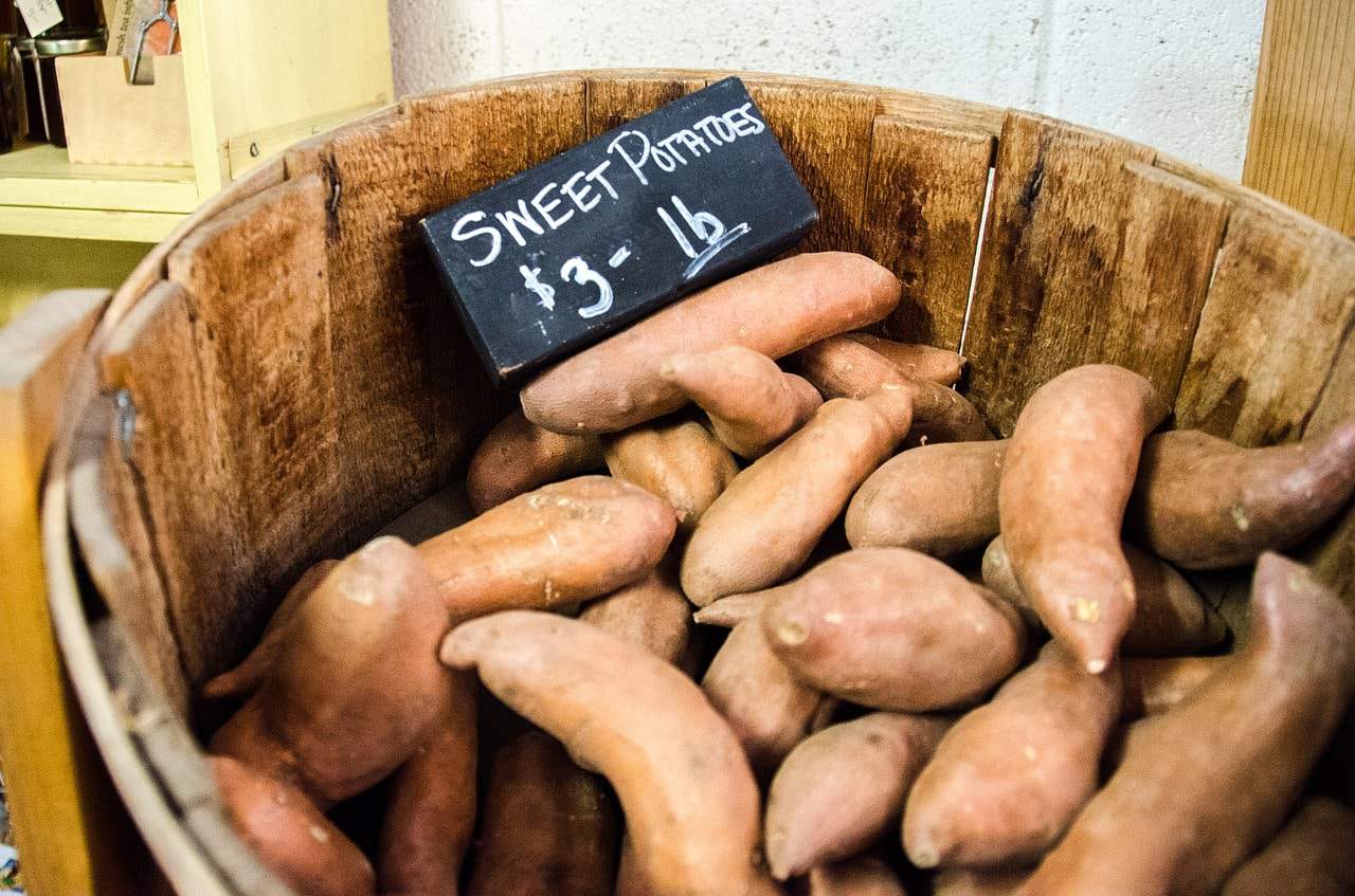 A Southeastern staple, sweet potatoes are displayed in a rustic wooden bucket accompanied by a charming sign.