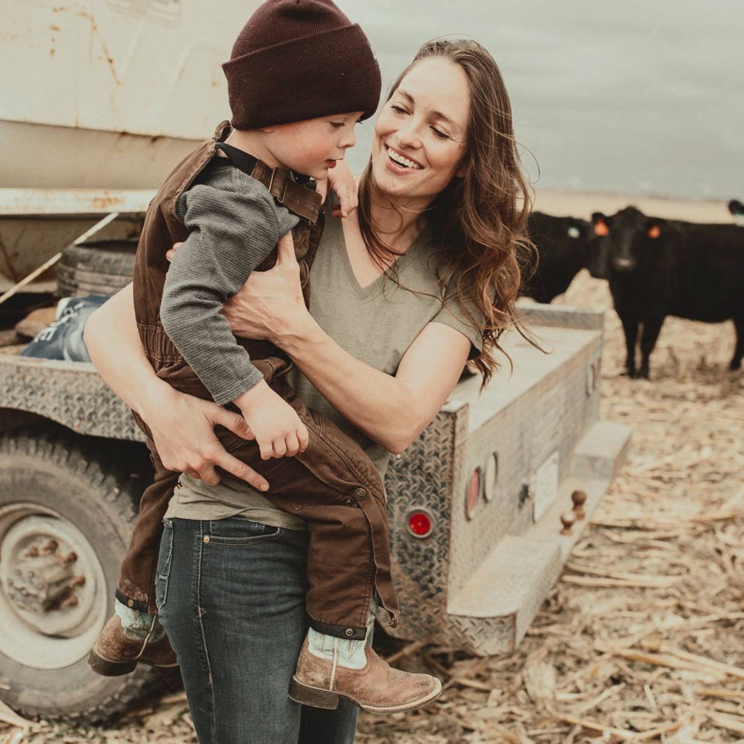 Natalie Kovarik holding her son in front of cattle on her Nebraska cattle ranch