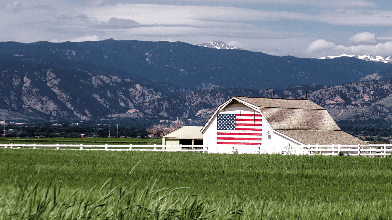 A white barn in a green field with mountains in the background, located on a beautiful farm.