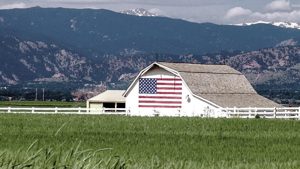 A barn with an american flag in the middle of a field, highlighting the patriotic spirit of America and its agricultural heritage.