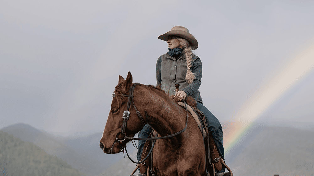 A woman riding a horse in front of a rainbow, showcasing the beauty of nature.