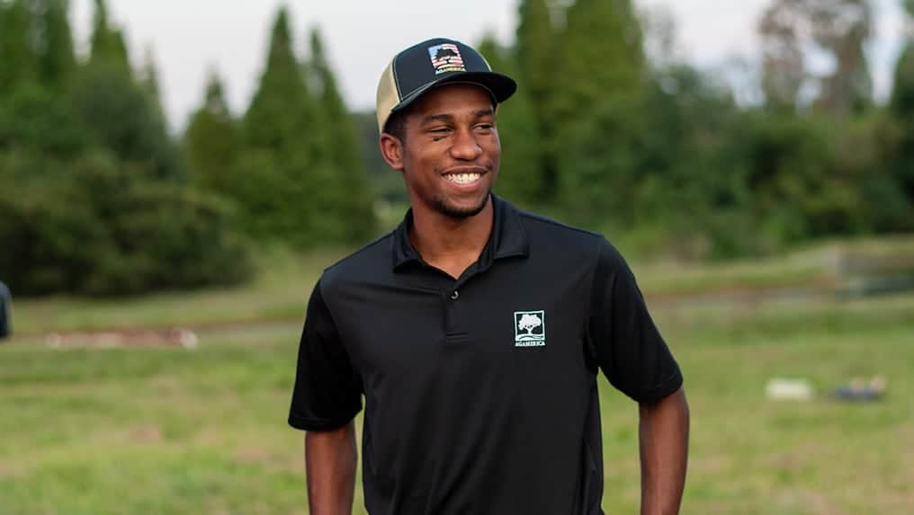 Man in a black polo shirt and cap, participating in an Ag Internship, smiling outdoors.