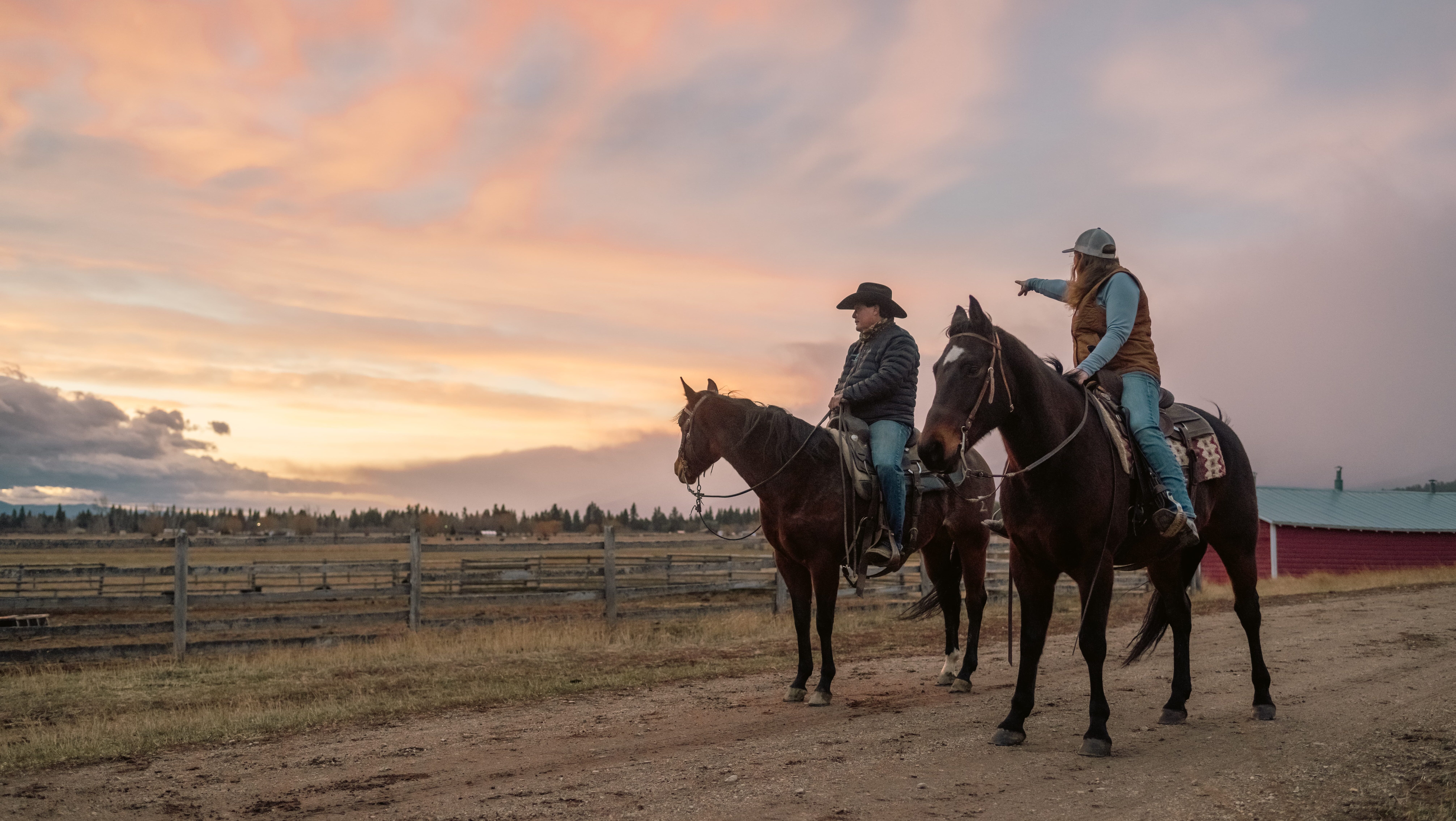 As the sun sets, two people on horseback ride along a dirt path, embodying the spirit of American agriculture. One rider points toward the horizon, evoking a scene reminiscent of findings from the 2022 Ag Census that highlight this enduring way of life.