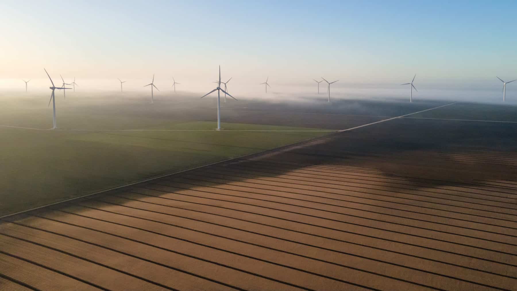 Aerial view of a wind farm with multiple wind turbines amidst fog, seamlessly integrating renewable energy into agricultural fields.