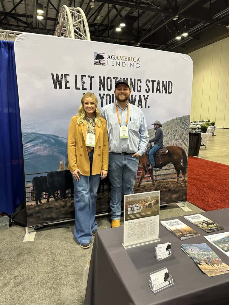 Two people stand at the AgAmerica Lending booth, featuring western imagery and materials on display. Clay Tucker is present, ready to share insights about AgAmerica’s agricultural financing solutions at this indoor event.
