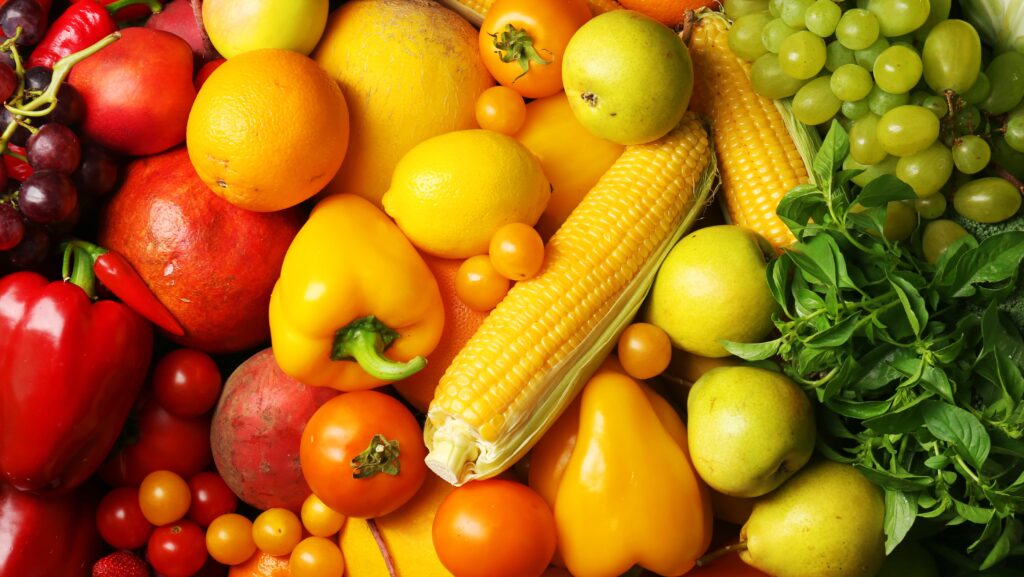 Assorted fruits and vegetables—including corn, bell peppers, tomatoes, oranges, grapes, apples, and leafy greens—are arranged closely together, showcasing the abundance supported by U.S. food policy and local agriculture.