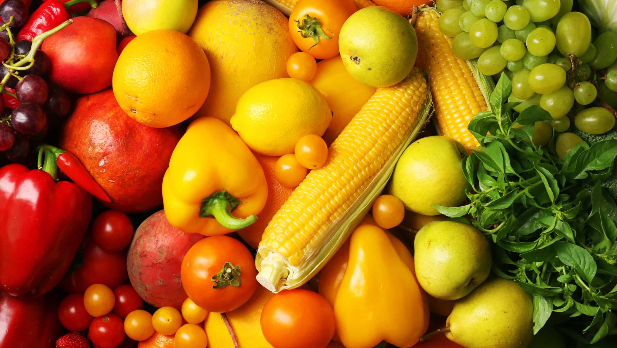 Assorted fruits and vegetables—including corn, bell peppers, tomatoes, oranges, grapes, apples, and leafy greens—are arranged closely together, showcasing the abundance supported by U.S. food policy and local agriculture.