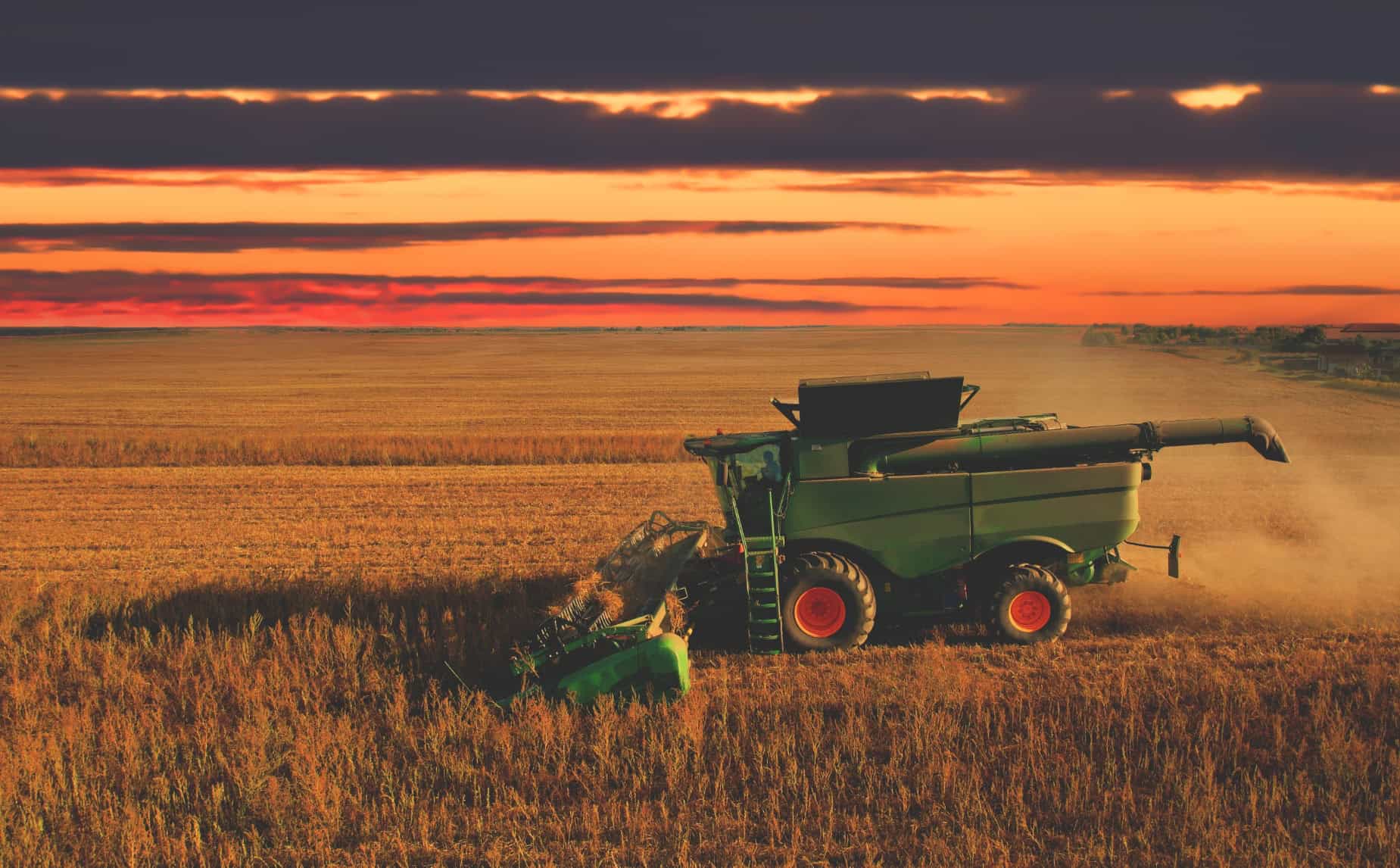 A combine harvester moves through a large field at sunset, cutting crops beneath an orange and purple sky—a striking image of U.S. agricultural trade powering the nation’s farms.